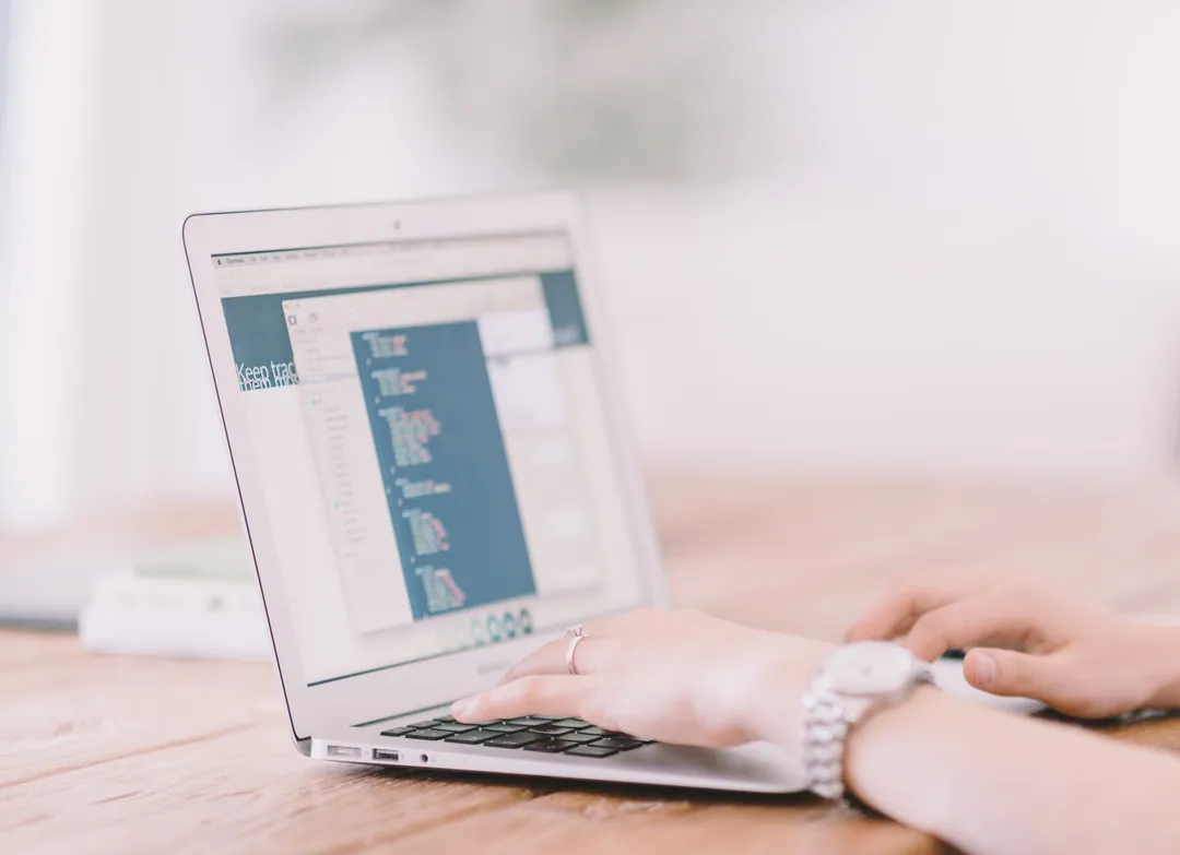 Laptop dengan editor kode di meja kerja bersama buku catatan dan ponsel